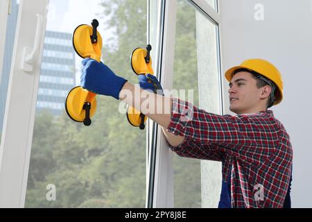 Worker using suction lifters during plastic window installation indoors Stock Photo