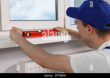 Worker using bubble level after plastic window installation indoors Stock Photo