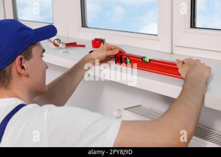 Worker using bubble level after plastic window installation indoors Stock Photo