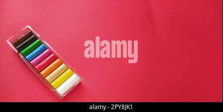 Multi-colored new plasticine in plastic packaging on a red background. Plasticine plates of red, pink, green, white, yellow, brown, blue, black. Set for children's creativity Stock Photo