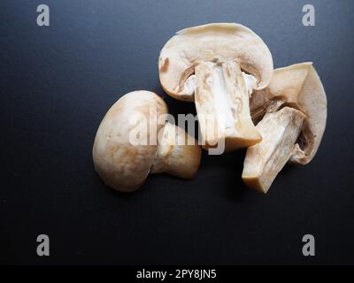 Champignons on a black background. Sliced and whole fresh uncooked raw mushrooms. Cooking mushrooms with a recipe. Stock Photo