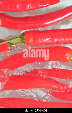 Red chilli peppers close-up in liquid with bubbles. Slices of red chilli peppers in water. Close-up of red chilli peppers on white background. Vertical and macro image Stock Photo