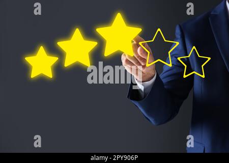 Man pointing at icons of stars on grey background, closeup. Quality rating Stock Photo