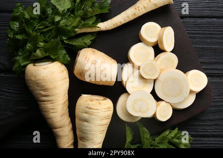 Whole and cut parsnips on black wooden table, flat lay Stock Photo
