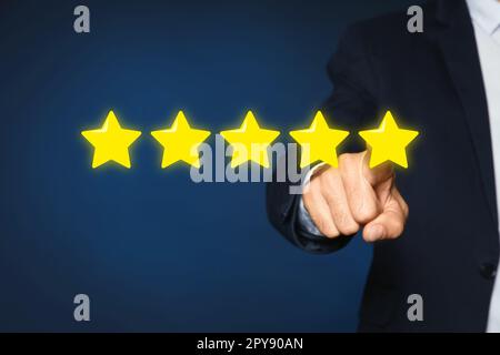 Man pointing at icons of five stars on blue background, closeup. Quality rating Stock Photo