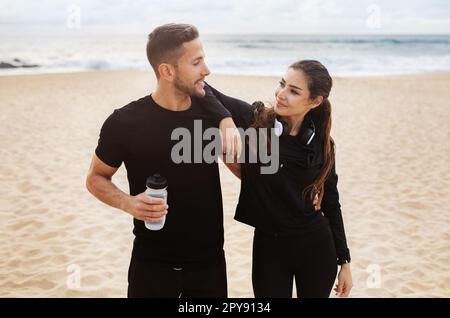 Young european man and woman in sportswear hugging, taking break during workout in morning on beach by ocean Stock Photo
