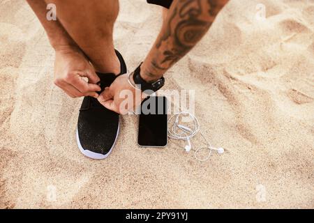 Runner man tying running shoes laces getting ready for run with smartphone and earphones near him, mockup, copy space Stock Photo