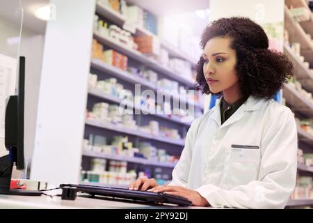 Checking which prescriptions are ready for refills. a pharmacist working on a computer in a pharmacy. Stock Photo
