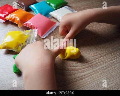 Children's hands crumple soft plasticine. Packages with plasticine are on the table. Creativity for the development of fine motor skills of hands. Creating a mold or model from plasticine Stock Photo