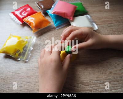 Children's hands crumple soft plasticine. Packages with plasticine are on the table. Creativity for the development of fine motor skills of hands. Creating a mold or model from plasticine Stock Photo