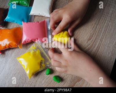 Children's hands crumple soft plasticine. Packages with plasticine are on the table. Creativity for the development of fine motor skills of hands. Creating a mold or model from plasticine Stock Photo