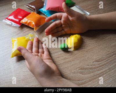 Children's hands crumple soft plasticine. Packages with plasticine are on the table. Creativity for the development of fine motor skills of hands. Creating a mold or model from plasticine Stock Photo
