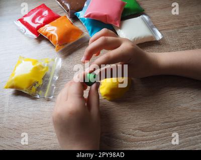 Children's hands crumple soft plasticine. Packages with plasticine are on the table. Creativity for the development of fine motor skills of hands. Creating a mold or model from plasticine Stock Photo