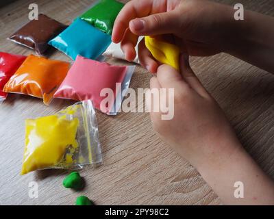 Children's hands crumple soft plasticine. Packages with plasticine are on the table. Creativity for the development of fine motor skills of hands. Creating a mold or model from plasticine Stock Photo