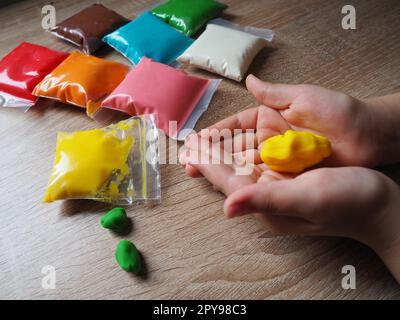 Children's hands crumple soft plasticine. Packages with plasticine are on the table. Creativity for the development of fine motor skills of hands. Creating a mold or model from plasticine Stock Photo