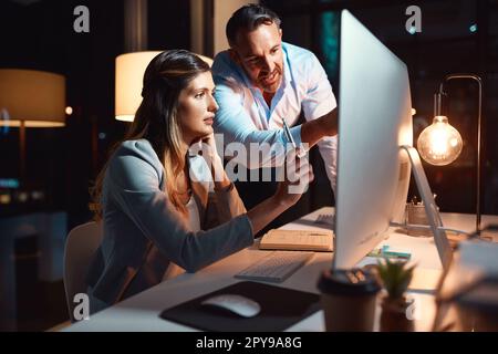 You wont find a more dedicated team. a businessman and businesswoman using a computer during a late night at work. Stock Photo