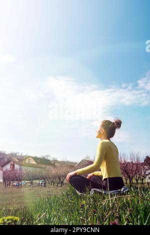 Woman meditating outdoors in countryside, yoga on green grass in village. Stock Photo