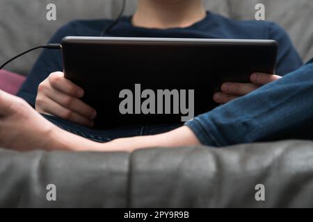Digital tablet computer in male hands, from below view closeup. Guy sitting on sofa play videogame on handheld gadget. Stock Photo