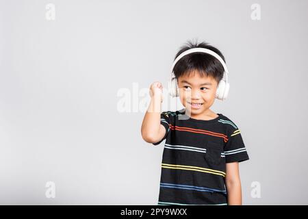 Little cute kid boy 5-6 years old listen music in wireless headphones in studio shot isolated. Stock Photo