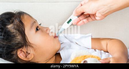 Mother parent checking temperature of her sick daughter with digital thermometer in mouth Stock Photo