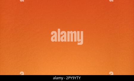 A sheet of thick paper of bright orange color. Close-up. Background intense shade. Natural lateral lighting. Fine cardboard or paper texture. Light gradient in degree of illumination. Copy space. Stock Photo