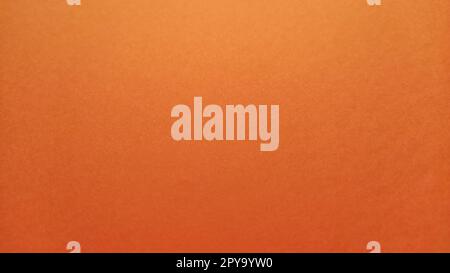 A sheet of thick paper of bright orange color. Close-up. Background intense shade. Natural lateral lighting. Fine cardboard or paper texture. Light gradient in degree of illumination. Copy space Stock Photo