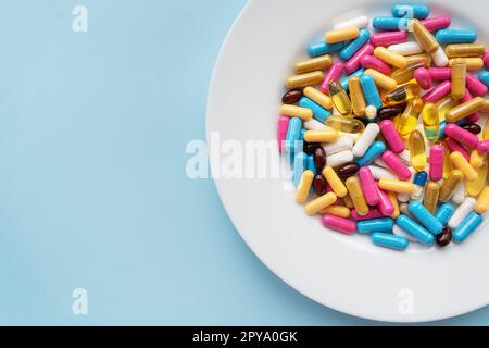 Colorful pills in a large white bowl on a blue background. The concept of health and evidence-based medicine. Stock Photo