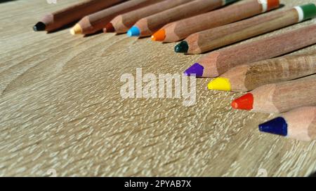 Multi-colored wooden pencils of a triangular shape in a section are intended for the development of fine motor skills of the child's hand. Pencils lie on a wooden table Stock Photo