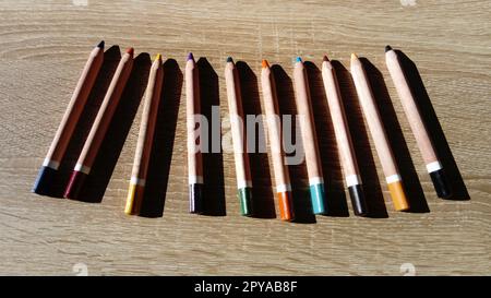 On a wooden table are wooden thick colored pencils. Hard light Stock Photo