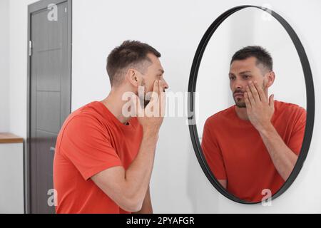 Sleep deprived man looking at himself in mirror indoors Stock Photo