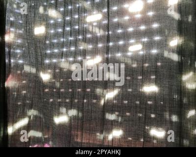 Sunlight shines through blinds with small holes and gray curtains - tulle. Abstract image. Summer mood. Reflection of light spots on fabric. Stock Photo