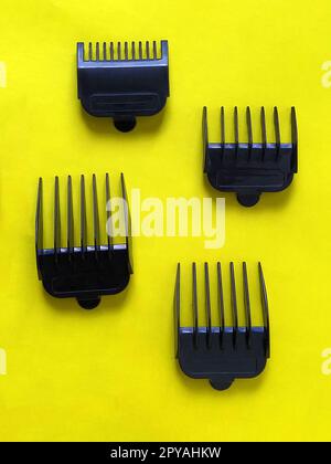 Nozzles for hair clippers. Four black plastic combs - a limiter for measuring the length of the cut hair. Nozzles from 1 cm to 4 cm. Hairdresser tools on a yellow background. Hair Salon Equipment Stock Photo