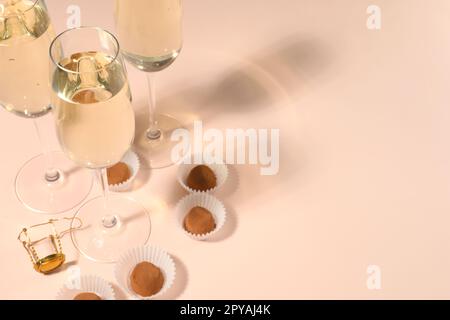 Glasses of delicious sparkling wine and chocolate truffles on pale pink background. Space for text Stock Photo