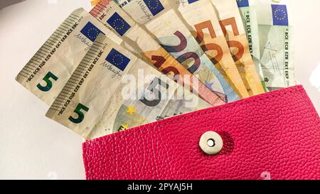 Euro paper notes. European currency on a white background. A purse or purse of bright pink color with a metal button, from which money is spread out in a fan. Banknotes of 5, 10, 20, 50 and 100 Stock Photo