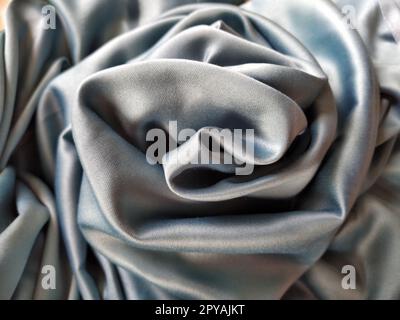 Silky to the touch fabric of gray - blue color with a brilliant shimmer. Natural lighting, light and shadow. The material is casually folded into a circle, resembling a rose bud. Polyester Textile Stock Photo