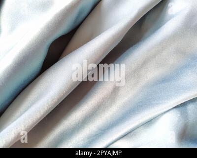 Silky to the touch fabric of gray - blue color with a brilliant shimmer. Natural lighting, light and shadow. The material is casually folded. Polyester Textile Stock Photo