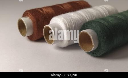 Bobbins and spools of thread of different colors - brown, white and green. Close-up. Natural light on the left side. Skeins of thread. Sewing supplies Stock Photo