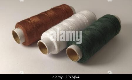 Bobbins and spools of thread of different colors - brown, white and green. Close-up. Natural light on the left side. Skeins of thread. Sewing supplies Stock Photo