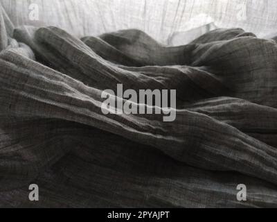 Light translucent curtains or tulle in the Scandinavian style. Gray pleated fabric or wrinkled textile hangs down. Close-up. The bottom edge of the curtain lies on a horizontal surface. Soft focus. Stock Photo