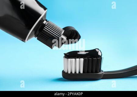 Applying charcoal toothpaste on brush against light blue background, closeup Stock Photo