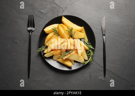 Served tasty baked potato wedges and rosemary on black table, flat lay Stock Photo