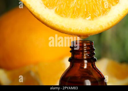Dripping essential oil from orange into bottle on blurred background, closeup. Space for text Stock Photo