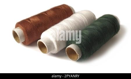 Bobbins and spools of thread of different colors: brown, white and green. Close-up. Natural light on the left side. Isolate on a white background with a light shadow. Skeins of thread. Sewing supplies Stock Photo