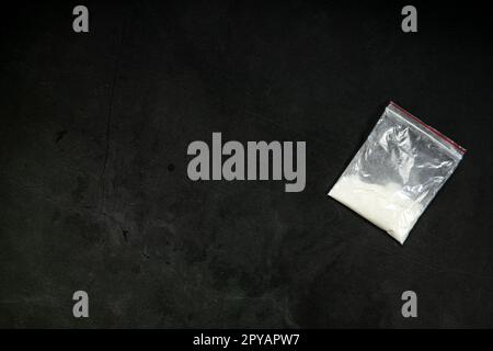 Cocaine powder lines, rolled banknote and drugs in plastic bag pocket on black glass surface background, top view. Drug addiction concept Stock Photo