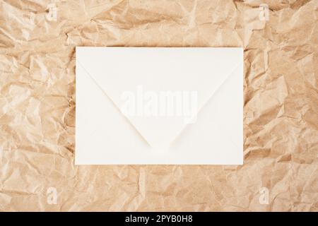 Background image crumpled recycled textured kraft paper with white cardboard envelope in middle. Top view, copy space Stock Photo