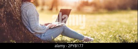 Woman with laptop sitting on the grass in the natural park. Stock Photo