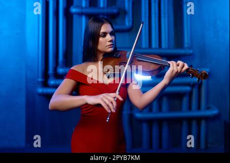 Young pretty woman playing violin solo over loft interior background Stock Photo