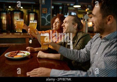 Cheerful friends drinking draft beer at bar table in pub Stock Photo