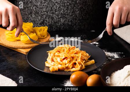 A close-up of hands holding a fork, digging into a plate of fast food in a kitchen. Stock Photo