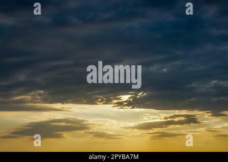 Sunset sky with warm-toned clouds in lower half and dark blue clouds in upper half creates a striking visual contrast in this photo. Stock Photo